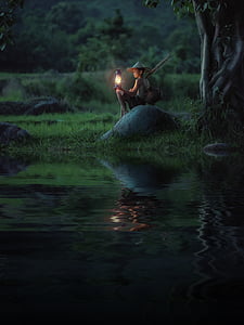boy holding kerosene lamp sitting on stone near river thumbnail