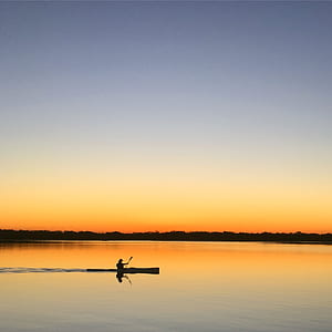 Silhouette of Man Inside of Boat Sailing on Body of Water during Sunset thumbnail