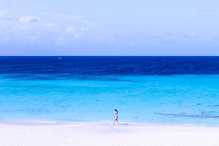 woman walking on beach beside wide body of water during daytime thumbnail