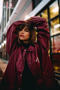 woman putting her hands behind her head standing in front of white and black building during daytime thumbnail