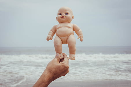 person holding baby doll near seashore thumbnail