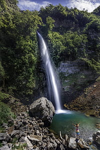 person standing facing waterfall between mountain thumbnail