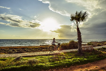 woman cycling beside sea during sunset thumbnail