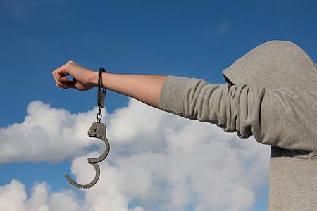 person in gray hoodie with handcuffs during daytime thumbnail