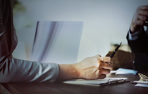 person holding black pen sitting near table thumbnail