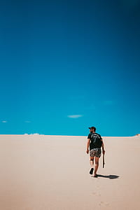 man walking on desert while holding stick under blue sky thumbnail