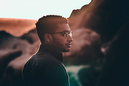 selective focus photography of man standing while wearing black top and eyeglasses thumbnail