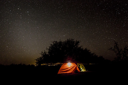 silhouette of person inside red and brown dome tent near tree with stars during night thumbnail