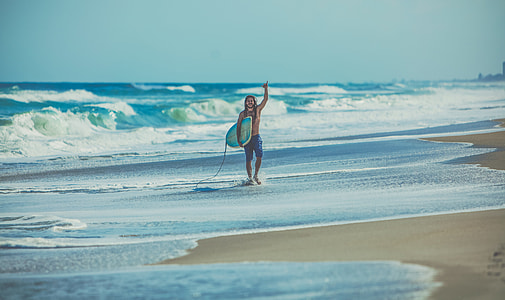 person waving and holding white and blue surfboard thumbnail
