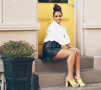 woman in white top and blue denim skirt sitting on stairs in front of yellow door thumbnail