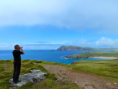man standing on gray rock formation while using binoculars at daytime thumbnail