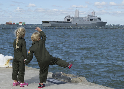 two girls in black suit standing in front of sea watching grey ship under white skies thumbnail