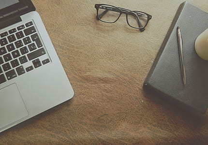 Macbook Pro Beside Black Framed Eyeglasses on Brown Wooden Surface thumbnail