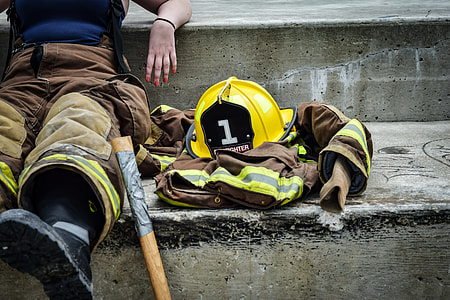 person in brown and yellow firefighter suit seating on concrete ground near yellow safety helmet during daytime thumbnail