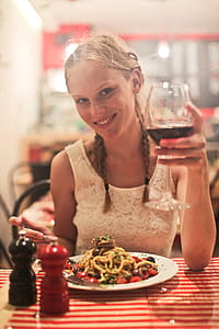 Two young blonde women drinking red wine in a restaurant with pasta on the table thumbnail