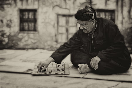 grayscale photography of man playing checkers thumbnail