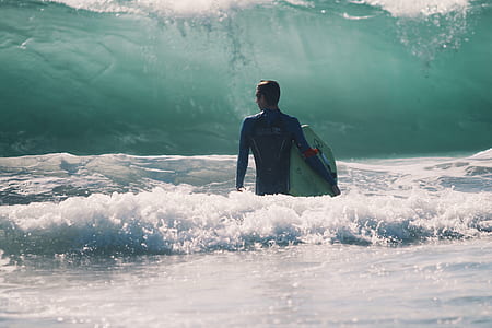 man in blue wet suit carrying a surf board thumbnail