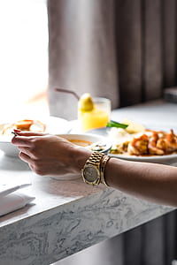 woman wearing round gold-colored watch while holding silver-colored utensil near cooked dishes thumbnail