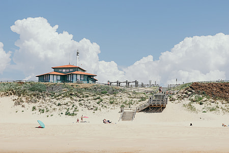 people in beach near brown stairs in distant of blue and brown structures thumbnail