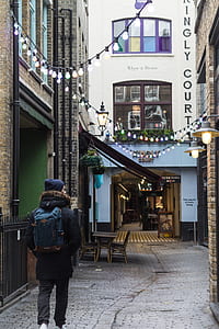man in black coat and blue backpack walking on gray pavement thumbnail