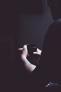 lowlight photography of man holding mug thumbnail