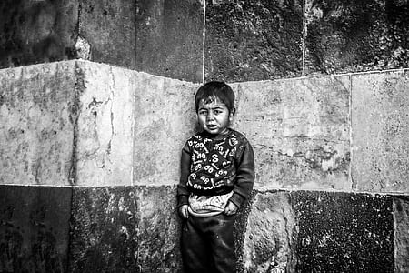 grayscale photo of boy standing at corner of wall thumbnail