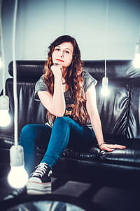 woman in gray top and blue jeans sitting on black leather couch thumbnail