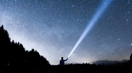 silhouette of man holding flashlight pointing in sky during night thumbnail