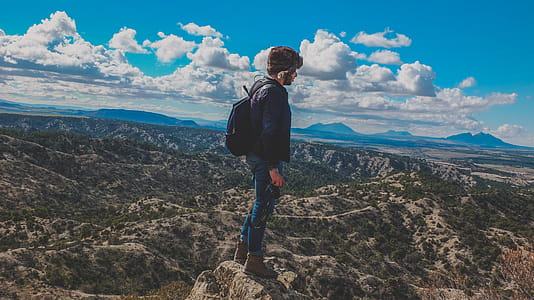 Man Wearing Blue Jeans Standing on Gray Stone Fragment Under Cloudy Sky thumbnail