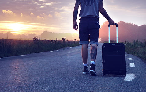 person holding black softside luggage standing on gray concrete road thumbnail