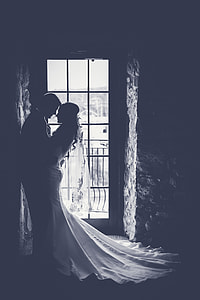 monochromatic photo of groom and bride embracing near door inside dim lit building thumbnail