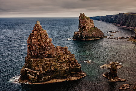 two brown rock formations in sea near cliffs thumbnail