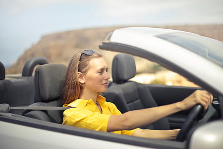 Young Woman Wearing Half-Sleeved Yellow Shirt Driving Convertible Silver Car thumbnail