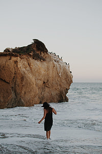 woman in black sleeveless bodycon mini dress and sun hat walking on seashore during daytime thumbnail