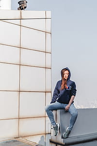 woman wearing blue Champion hoodie sitting on wall during daytime thumbnail