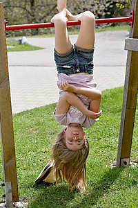 girl hanging upside down on red metal bar thumbnail