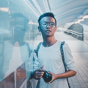 focus photo of man holding camera standing near wall thumbnail