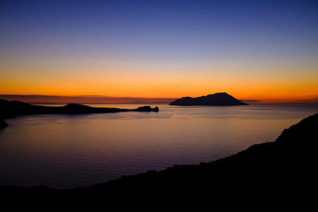 calm body of water surrounded by silhouette of mountains during golden hour thumbnail