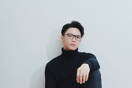 man wearing black framed eyeglasses and black turtleneck long-sleeved shirt leaning on white wall paint thumbnail