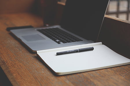 black pen on notebook beside laptop computer on brown wooden table thumbnail