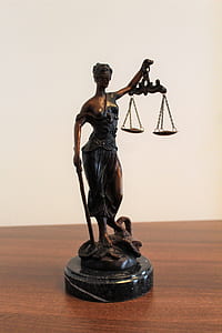person holding balance scale figurine on brown wooden surface thumbnail