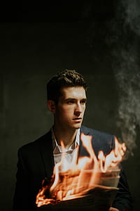 man wearing black blazer and white dress shirt holding newspaper with fire thumbnail