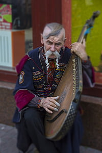 man playing brown wooden string instrument outdoors thumbnail