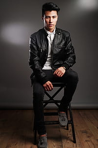 man wearing black leather zip-up jacket and pants sitting on stool thumbnail