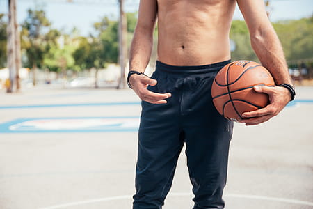 A young man in black sports pants holding a basketball in his left hand in the day time thumbnail