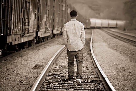 grayscale photo of man walking on train railway thumbnail