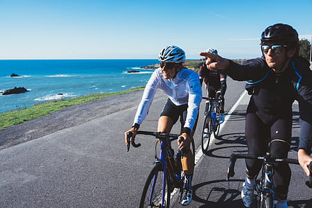 men riding bicycles beside ocean during daytime thumbnail