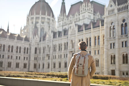 Man with backpack on his shoulders looking on white concrete building thumbnail