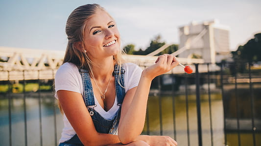 shallow focus photography of woman sitting beside the fence of the lake while holding lollipop thumbnail