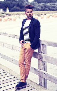 man wearing black notched lapel blazer and brown denim jeans while leaning on brown wooden fence during daytime thumbnail